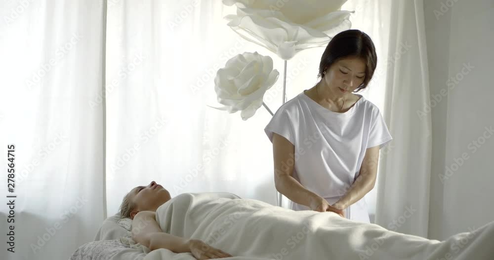 asian masseuse is stroking fingers, arm and head of relaxed female client, lying on table asian masseuse is stroking fingers, arm and head of relaxed female client, lying on table