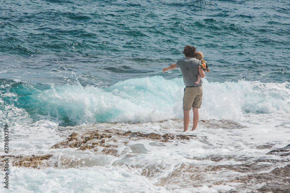 young father holding kid on hands showing waves in sea