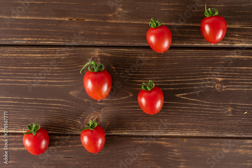 Group of six whole fresh red tomato cherry in line flatlay on brown wood