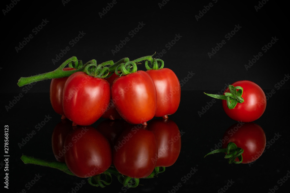 Group of five whole fresh red tomato cherry isolated on black glass