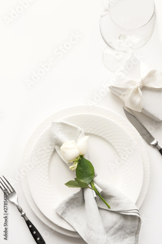 Romantic and wedding table setting with white rose, gift, dishware, silverware on white table.View from above.
