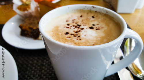 A cup of cappuccino coffee with foam and chocolate on top on wooden table background. it's a white ceramic cup in the morning breakfast