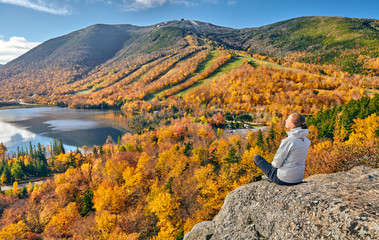 Woman hiking at Artist's Bluff in autumn. View of Echo Lake. Fall colours in Franconia Notch State Park. White Mountain National Forest, New Hampshire, USA