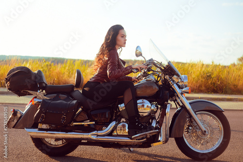Fototapeta Naklejka Na Ścianę i Meble -  Beautiful brunette in a red leather jacket on a motorcycle in the field. Girl with beautiful hair