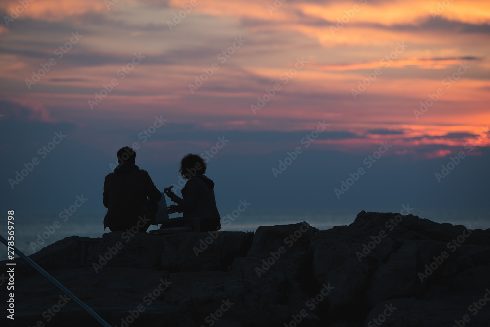 couple sitting on rocky cliff looking on sunset. romantic date