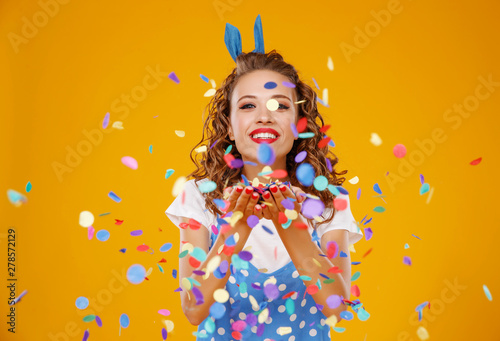 cheerful funny young woman with festive confetti on yellow .