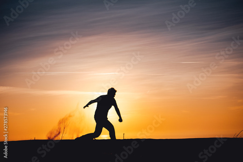 Side view of a active sport athlete man jumping and having fun in wide endless sand dunes at colorful, amazing sunset evening light. Lokken, Lønstrup in North Jutland in Denmark, Skagerrak, North Sea