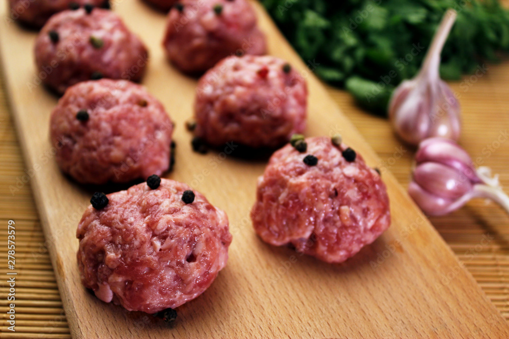 close up raw meatballs with peper beans on a cutting board on a background of a bamboo mat with garlic and parsley close up raw meatballs with peper beans on a cutting board on a background of a bamboo mat with garlic and parsley