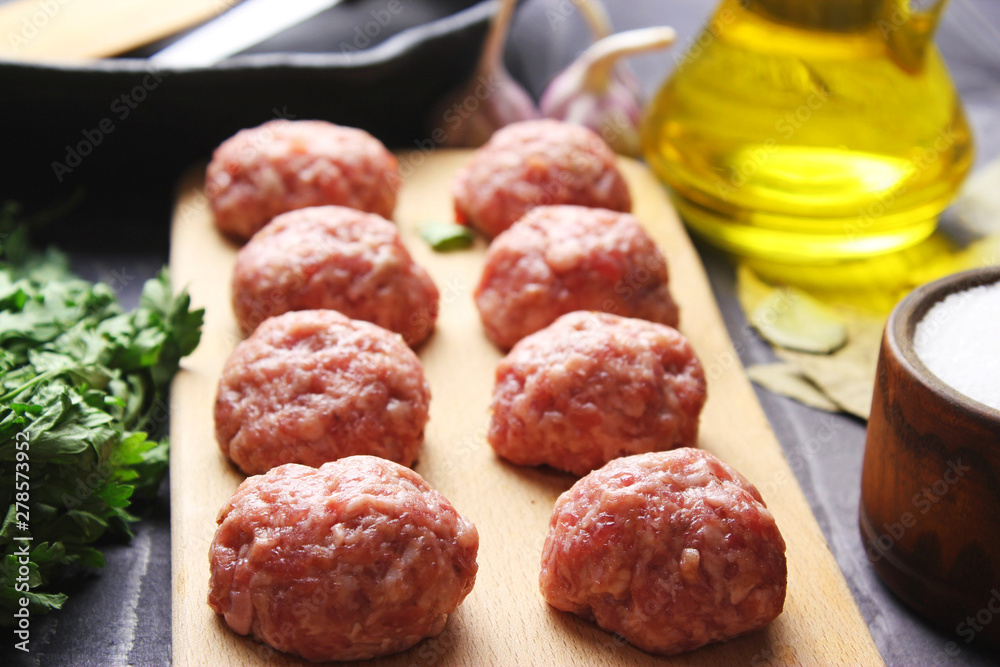 close up raw meatballs on a cutting board on a background of a bamboo mat with garlic and parsley