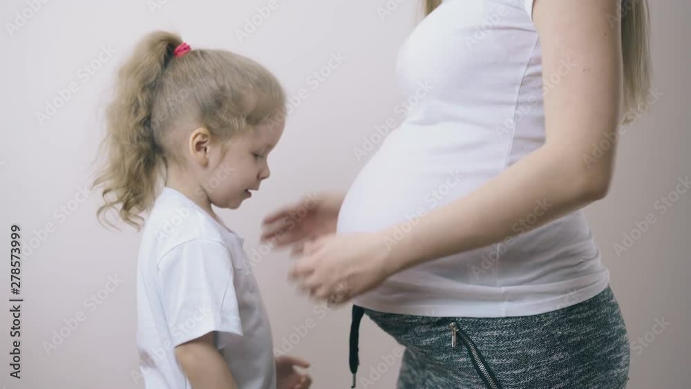 pretty little blonde curly haired girl hugs pregnant mommy large tummy waiting for brother or sister at home pretty little blonde curly haired girl hugs pregnant mommy large tummy waiting for brother or sister at home