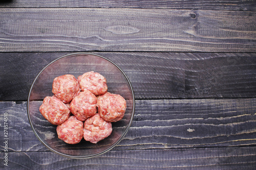 flat lay raw meat balls in a glass bowl on black wooden table top close up copy space