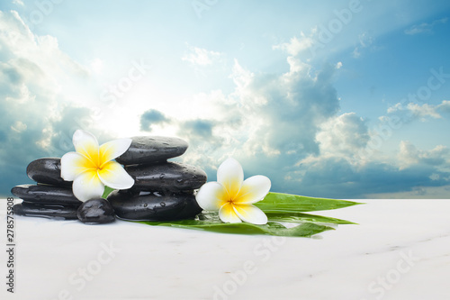 Tropical flowers and black stones ready for healthy therapy and clouds with sunlight. Health objects on white marble table