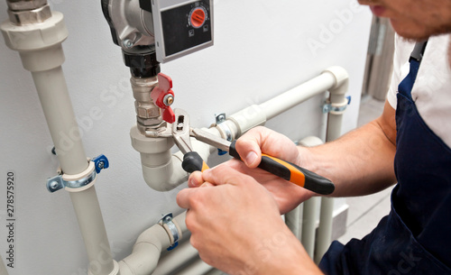 The man is installing the heater system in the house and checking pipes by the wrench photo