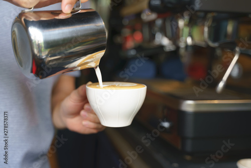 Hand pouring frothy steamed milk into coffee