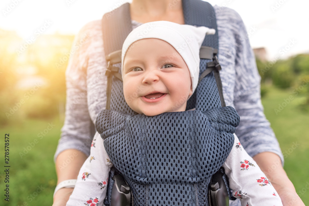 Young mother and her baby girl in a baby carrier. - obrazy, fototapety, plakaty 