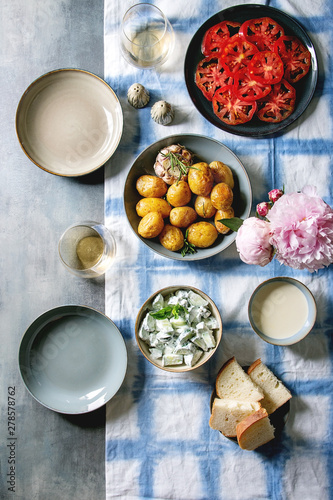 Summer vegetarian dinner table for family or friends. Young baked potatoes, tomato carpaccio, cucumber salad, bread, wine, sauce and flowers over linen tablecloth. Flat lay, space
