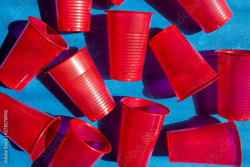 Red plastic cups on a blue background. Composition from empty plastic glasses. Many disposable beverage containers. View from above