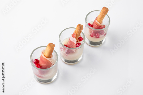 Cheese sticks wrapped in bacon with currants in a sauce in glasses. Beautifully decorated catering banquet menu. Food snacks and appetizers for buffet. Isolated on white background