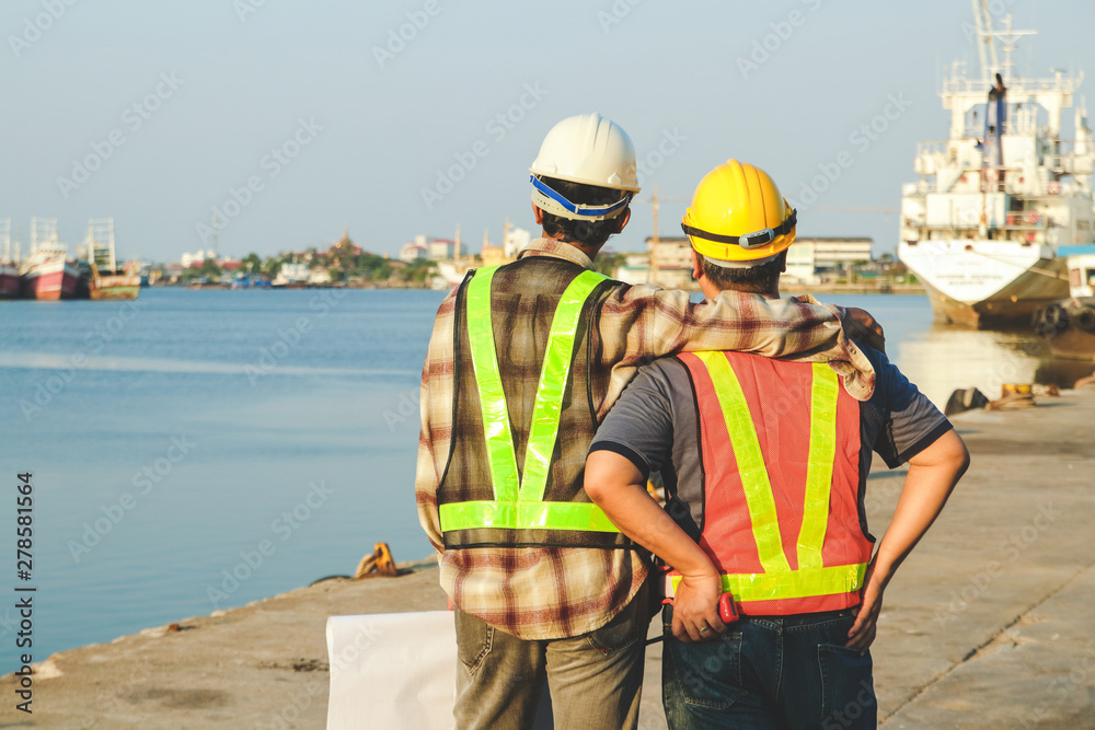 Engineers wearing white hats, carrying construction paper, hugging workers, wearing yellow hats Working at the port Engineers wearing white hats, carrying construction paper, hugging workers, wearing yellow hats Working at the port