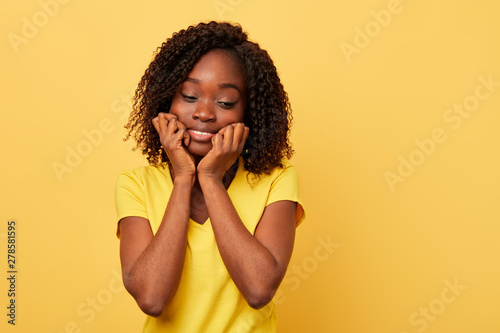 Obraz na plátně lovely, cute, beautiful serious woman looks down touches cheeks by hands fists isolated in yellow background