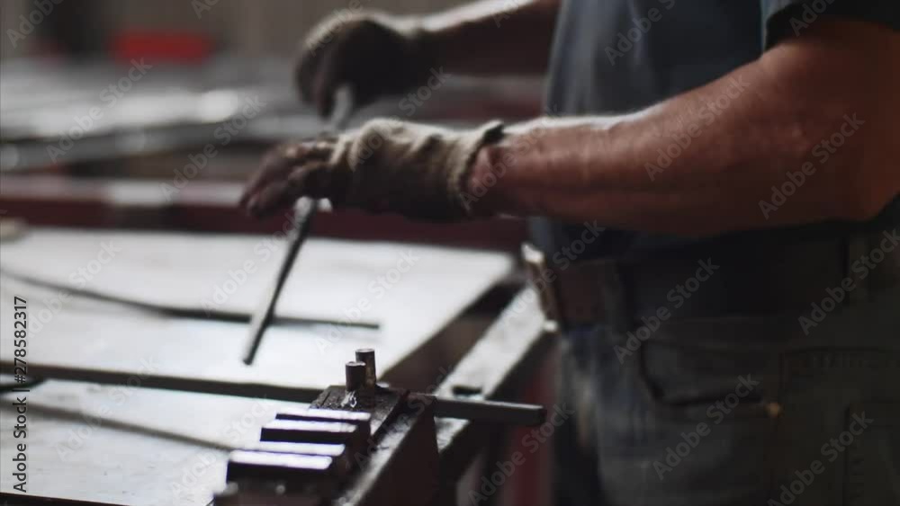 Locksmith at work in fitting shop, hands closeup. Master bends metal bar in vice on workplace for manufacture of metal structures. He compares two metal bars with each other in form. Locksmith at work in fitting shop, hands closeup. Master bends metal bar in vice on workplace for manufacture of metal structures. He compares two metal bars with each other in form.
