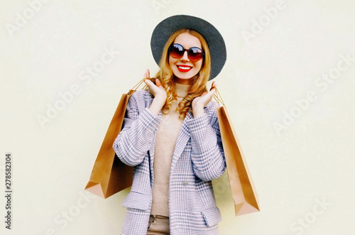 Portrait happy smiling woman with shopping bags in pink coat, round hat on wall background