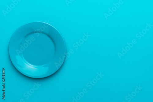 Image of round ceramic plate over turquoise blue background with copy space and left side position. Top view of blank dish on blue table.
