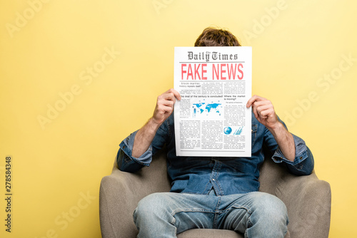 man sitting in armchair and reading newspapaper with fake news on yellow background