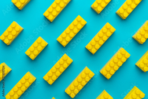 Top view of plastic blocks background. Flat lay image of toy background made with yellow building blocks from child constructor. Bright yellow plastic building blocks on turquoise blue background. photo