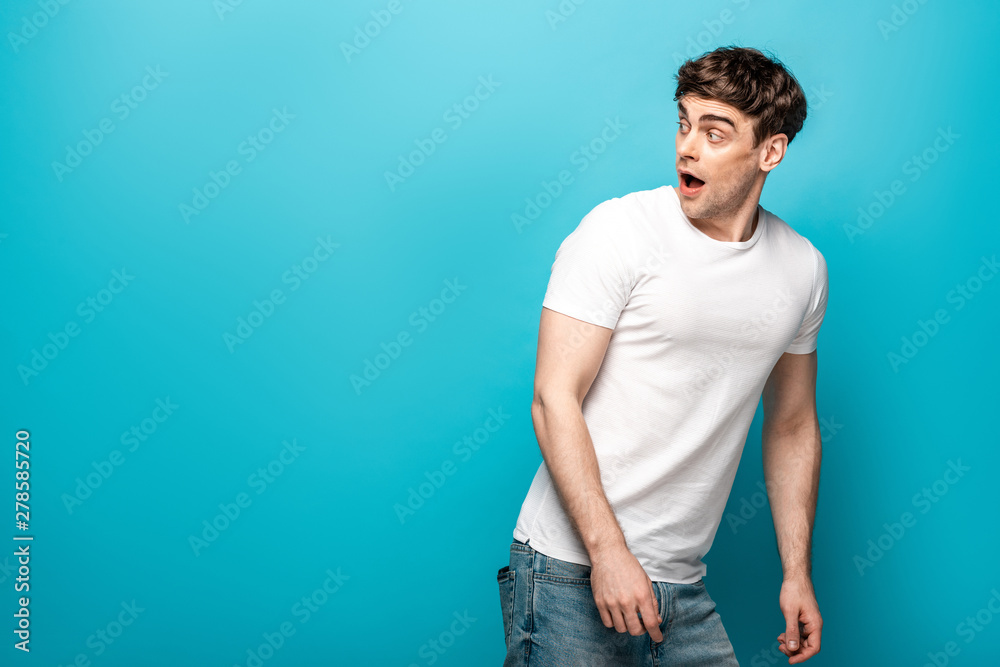 scared young man in white t-shirt looking back on blue background