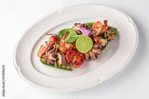 Luxurious seafood salad with shrimp, octopus, squid, fish, lime, cherry tomatoes, grilled vegetables and greens Banquet festive dishes. Fine dining restaurant menu. White background.