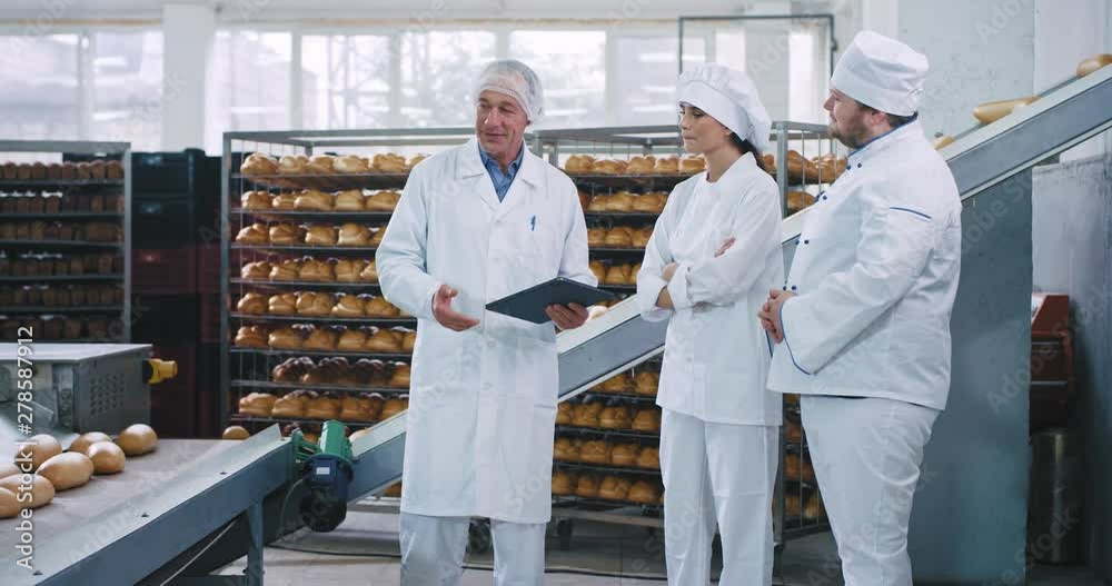 Attractive woman baker and her colleague baker have a chat with a old man engineer mechanic about the rules of using the industrial machine