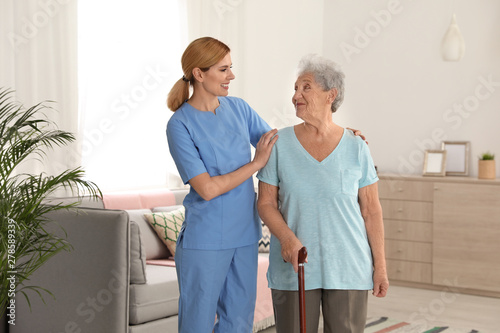 Nurse assisting elderly woman with cane indoors