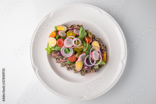 Delicious tuna salad in sesame, quail eggs, vegetables and dried olives. Nutritious healthy dish. Banquet festive dishes. Gourmet restaurant menu. White background.
