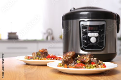 Plates with meat and garnish prepared in multi cooker on table in kitchen. Space for text