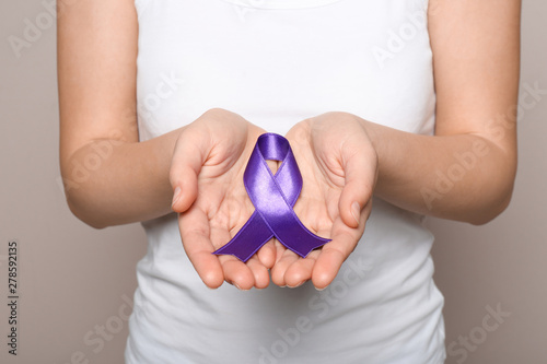 Woman holding purple ribbon on grey background, closeup. Domestic violence awareness photo