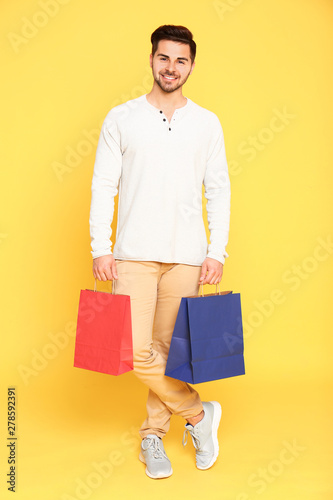 Full length portrait of young man with paper bags on yellow background