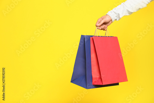Young man with paper bags on color background, closeup. Space for text