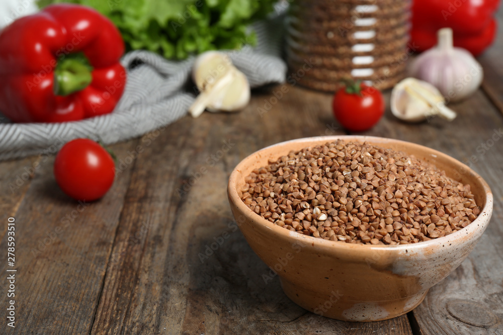 Ceramic bowl with uncooked buckwheat on wooden kitchen table. Space for text Ceramic bowl with uncooked buckwheat on wooden kitchen table. Space for text