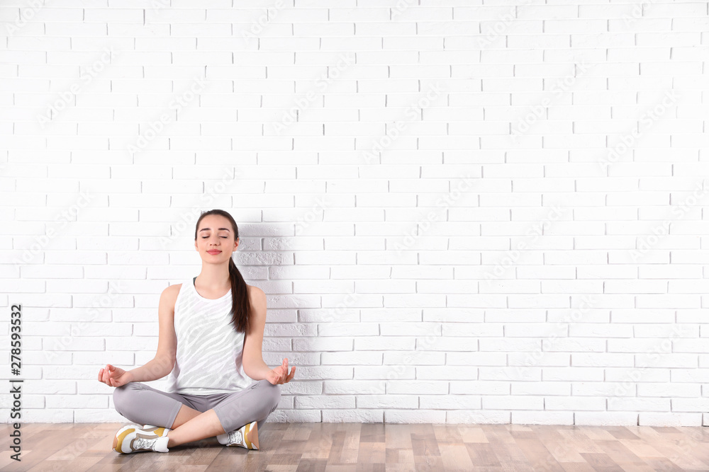 Young woman meditating on floor near brick wall, space for text. Zen concept