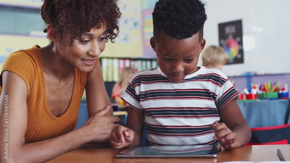 Elementary School Teacher And Male Pupil Drawing Using Digital Tablet In Classroom 