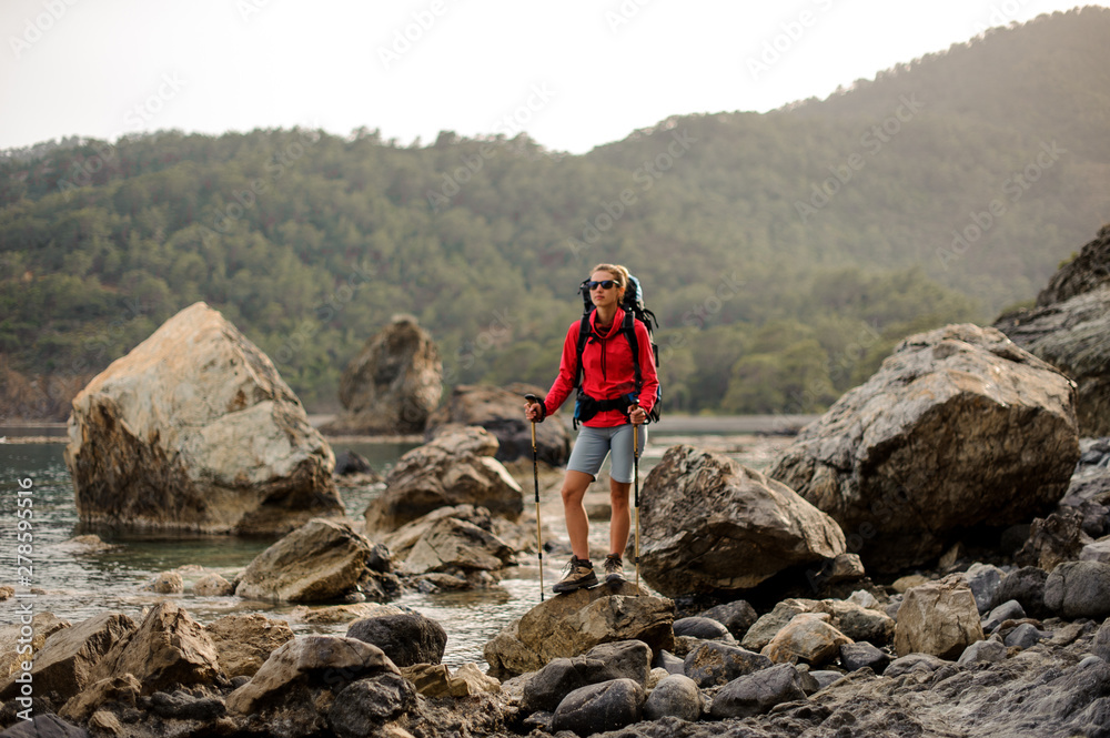 Woman with hiking equipment travels through rocky coast