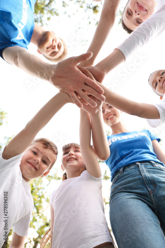 Low angle view of volunteers with kids joining hands in park