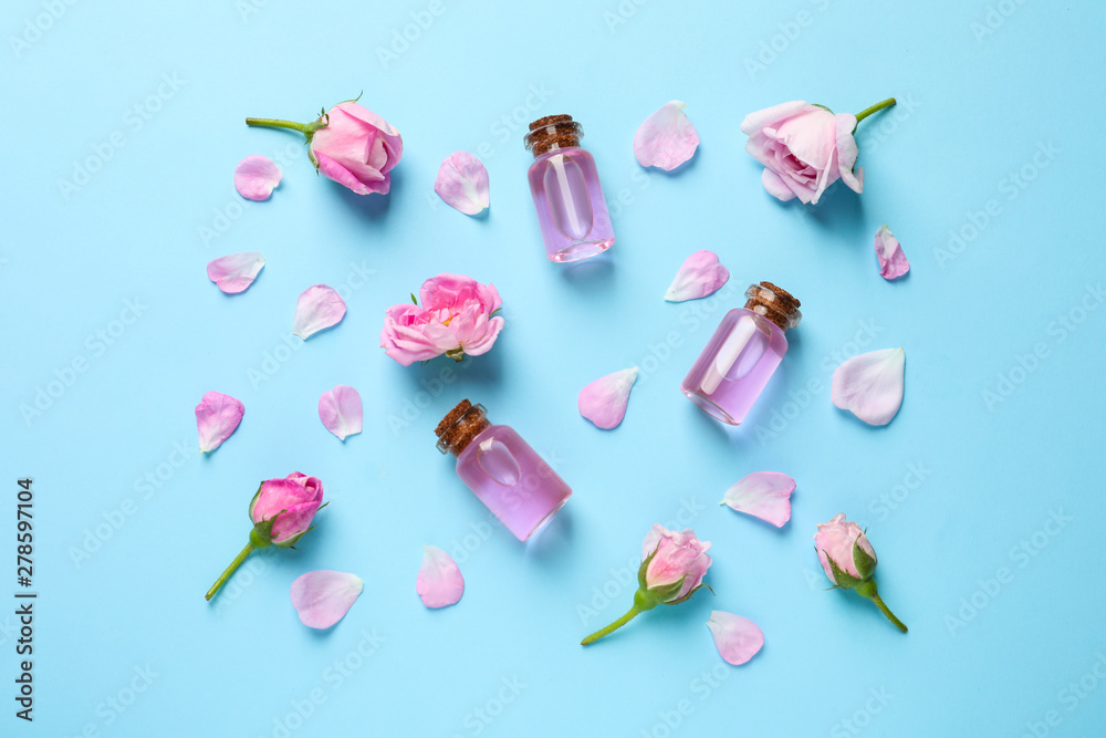 Fresh flowers, petals and bottles of rose essential oil on color background, flat lay