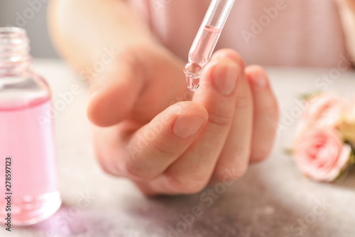 Woman dripping rose essential oil on finger at table  closeup