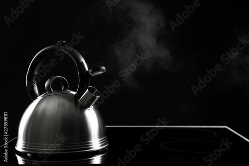 Modern kettle with whistle on stove against black background, space for text