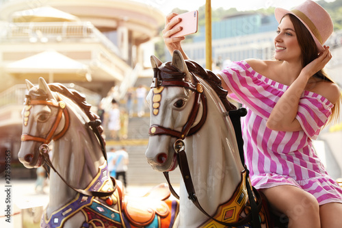 Young pretty woman taking selfie on carousel in amusement park © New Africa