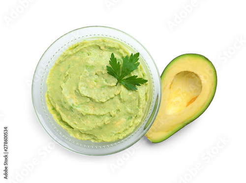 Glass bowl of tasty guacamole with parsley and cut avocado on white background, top view
