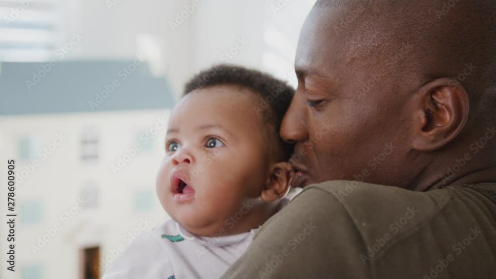 Over The Shoulder View Of Father Cuddling And Playing With Baby Son In Nursery At Home Over The Shoulder View Of Father Cuddling And Playing With Baby Son In Nursery At Home