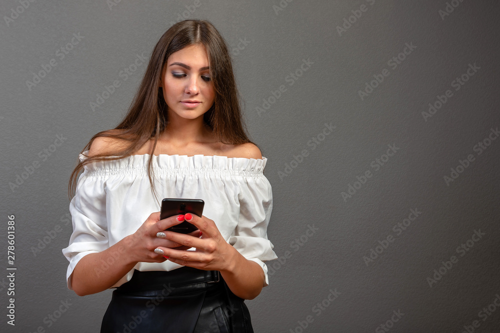 Photo of smiling woman with long dark hair holding and using black mobile phone isolated over gray background - image Photo of smiling woman with long dark hair holding and using black mobile phone isolated over gray background - image